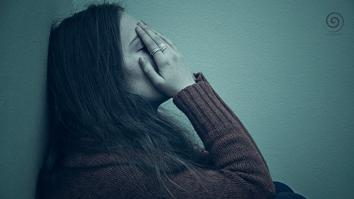 A sad woman sitting against the wall with her face in her hands